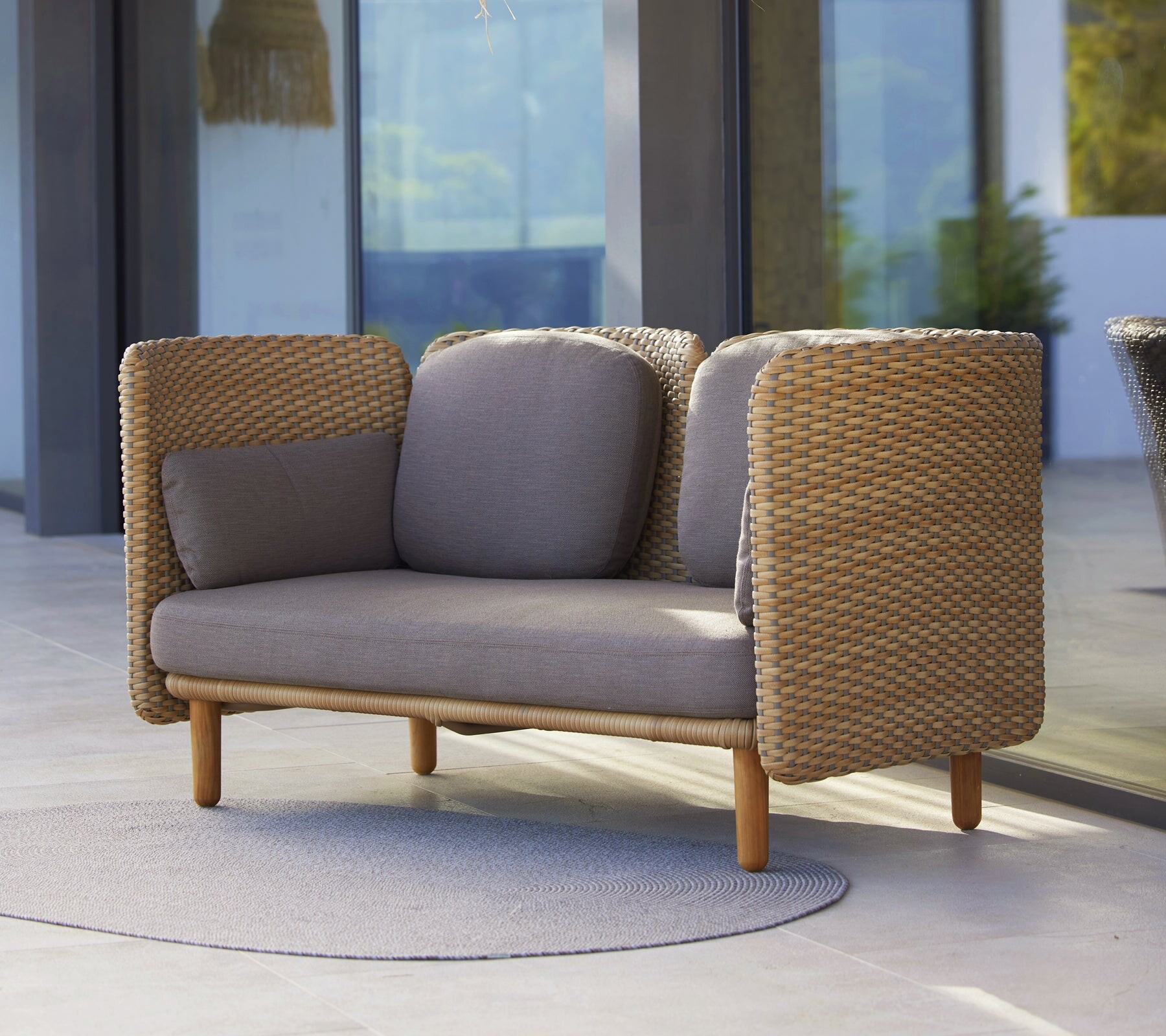 Cane-line Arch 2-seater sofa on a rug beside a glass house