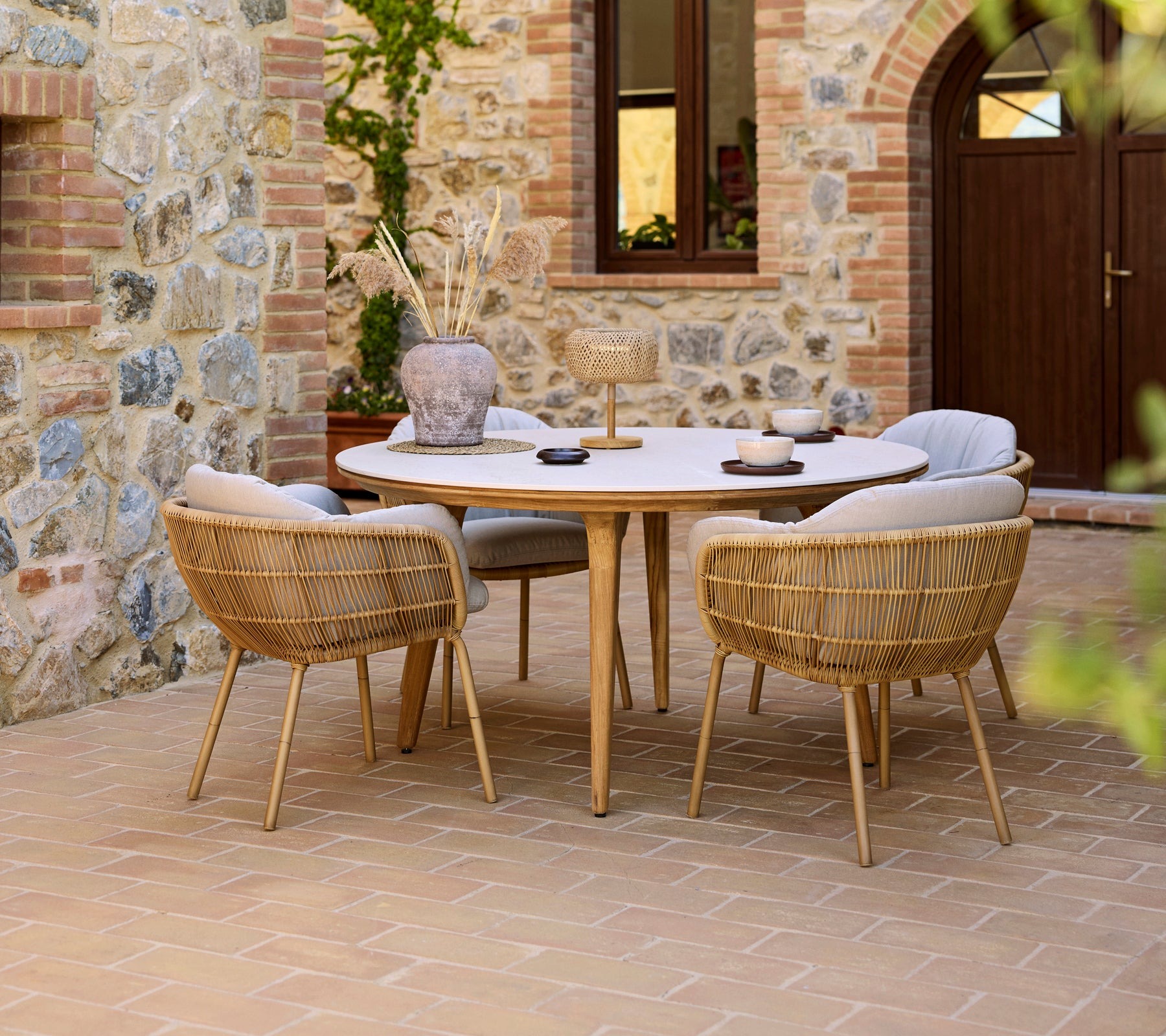 Cane-line Aspect round outdoor dining table with rope chairs in a stone courtyard