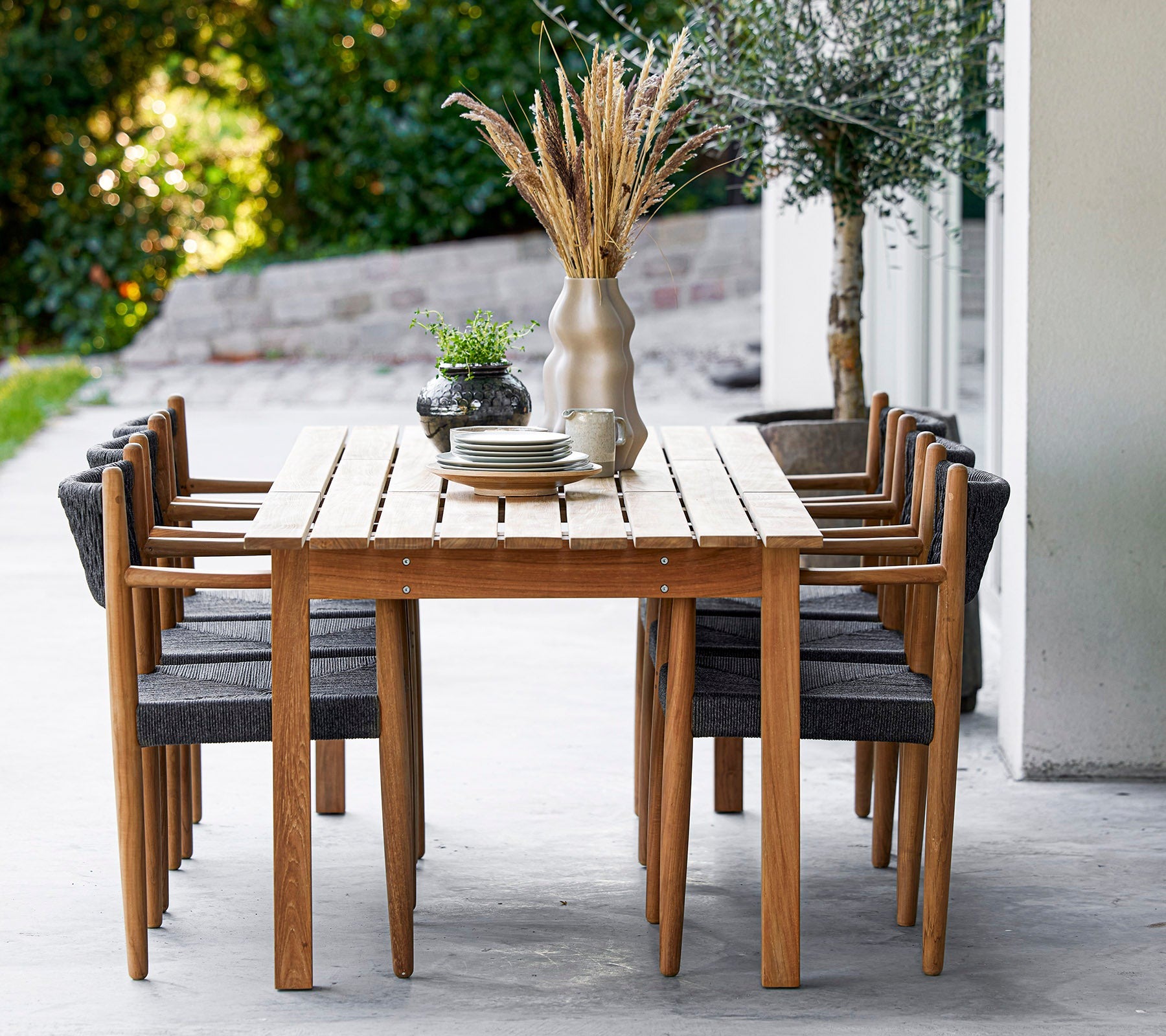 Cane-line Royal teak dining table and armchairs with dark rope backs on a terrace